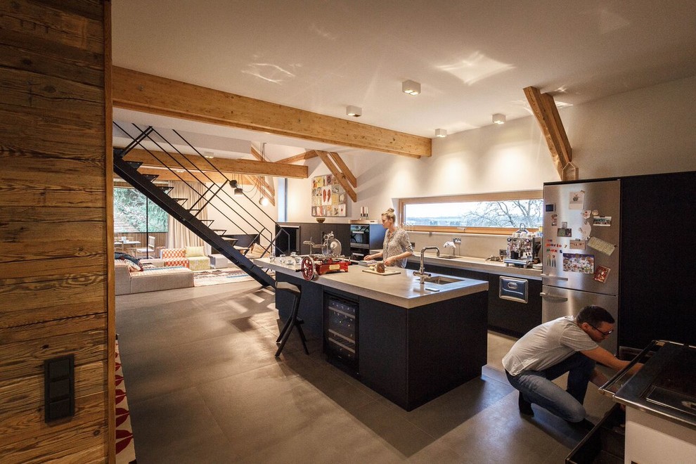 Photo of a large eclectic l-shaped open plan kitchen in Munich with ceramic floors, an undermount sink, flat-panel cabinets, black cabinets, grey splashback, stainless steel appliances and with island.