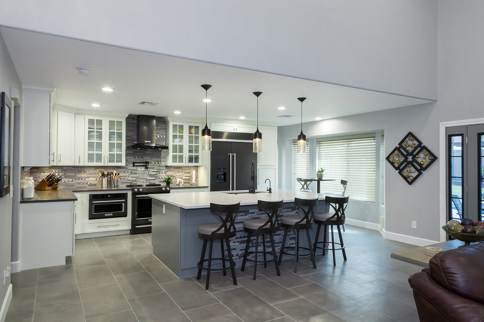Mid-sized transitional l-shaped porcelain tile and gray floor open concept kitchen photo in Phoenix with an undermount sink, shaker cabinets, white cabinets, quartz countertops, gray backsplash, glass tile backsplash, black appliances, an island and gray countertops