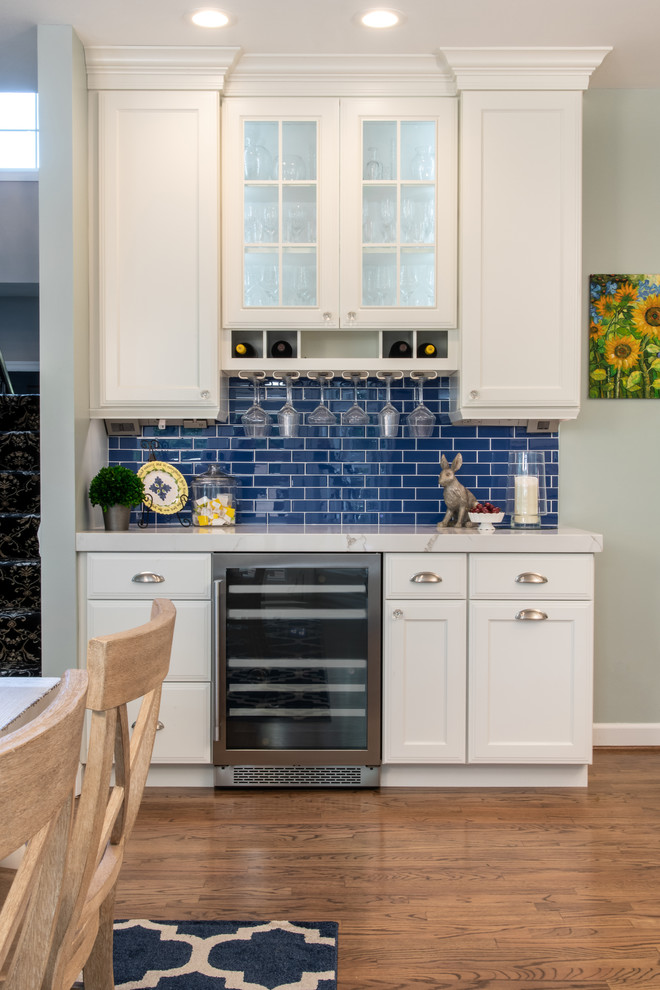 This is an example of a large traditional l-shaped eat-in kitchen in St Louis with recessed-panel cabinets, white cabinets, quartz benchtops, blue splashback, ceramic splashback, medium hardwood floors, with island and brown floor.