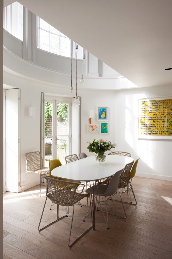 This is an example of a mid-sized eclectic dining room in London with white walls and brown floor.