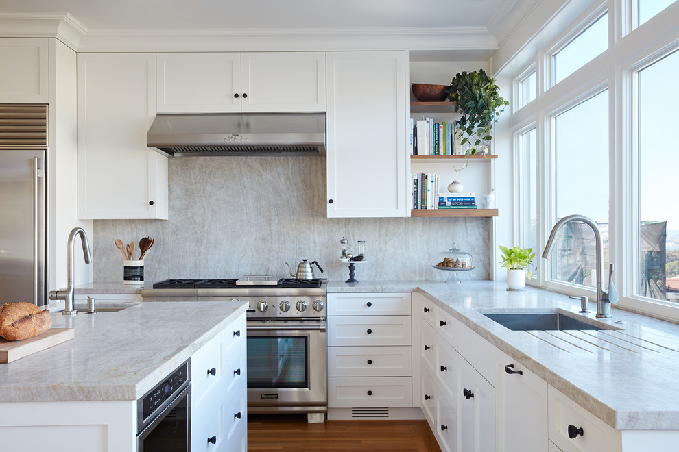 This is an example of a transitional u-shaped eat-in kitchen in San Francisco with an undermount sink, recessed-panel cabinets, white cabinets, quartzite benchtops, beige splashback, stone slab splashback, stainless steel appliances, medium hardwood floors, with island and orange floor.