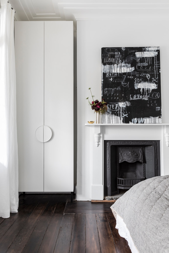 This is an example of a mid-sized modern guest bedroom in Sydney with white walls, dark hardwood floors, a standard fireplace and a metal fireplace surround.