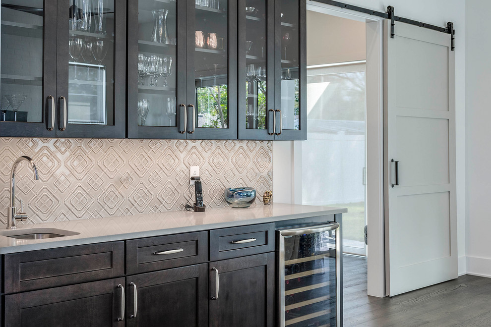 This is an example of a large transitional single-wall wet bar in Orlando with an undermount sink, glass-front cabinets, dark wood cabinets, marble benchtops, beige splashback, mosaic tile splashback, dark hardwood floors and multi-coloured benchtop.