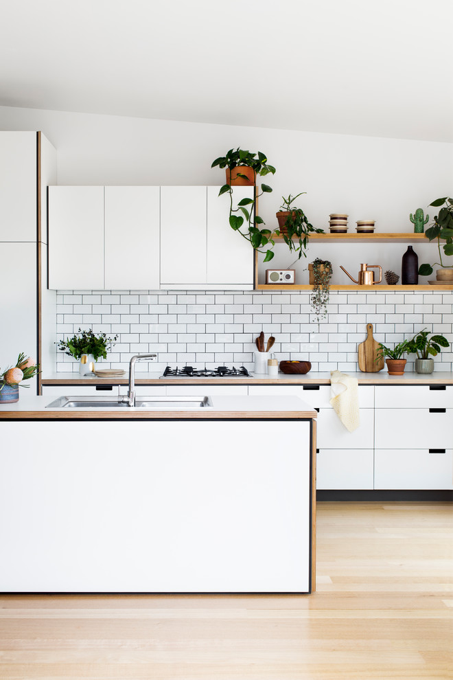 This is an example of a contemporary kitchen in Melbourne with a double-bowl sink, flat-panel cabinets, white cabinets, white splashback, subway tile splashback and light hardwood floors.
