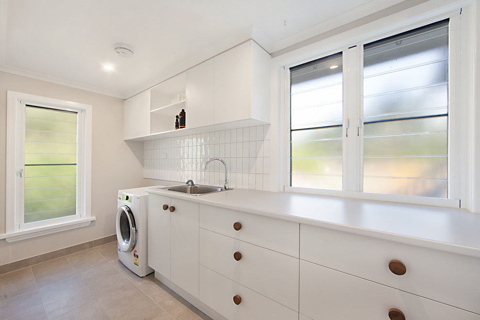 Inspiration for a mid-sized beach style galley utility room in Townsville with a drop-in sink, flat-panel cabinets, white cabinets, grey walls, ceramic floors, a side-by-side washer and dryer and beige floor.