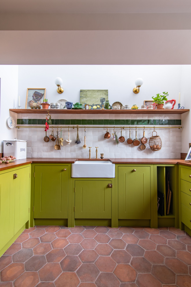 Photo of a medium sized contemporary u-shaped kitchen/diner in London with a belfast sink, green cabinets, wood worktops, white splashback, integrated appliances, terracotta flooring, no island and brown worktops.