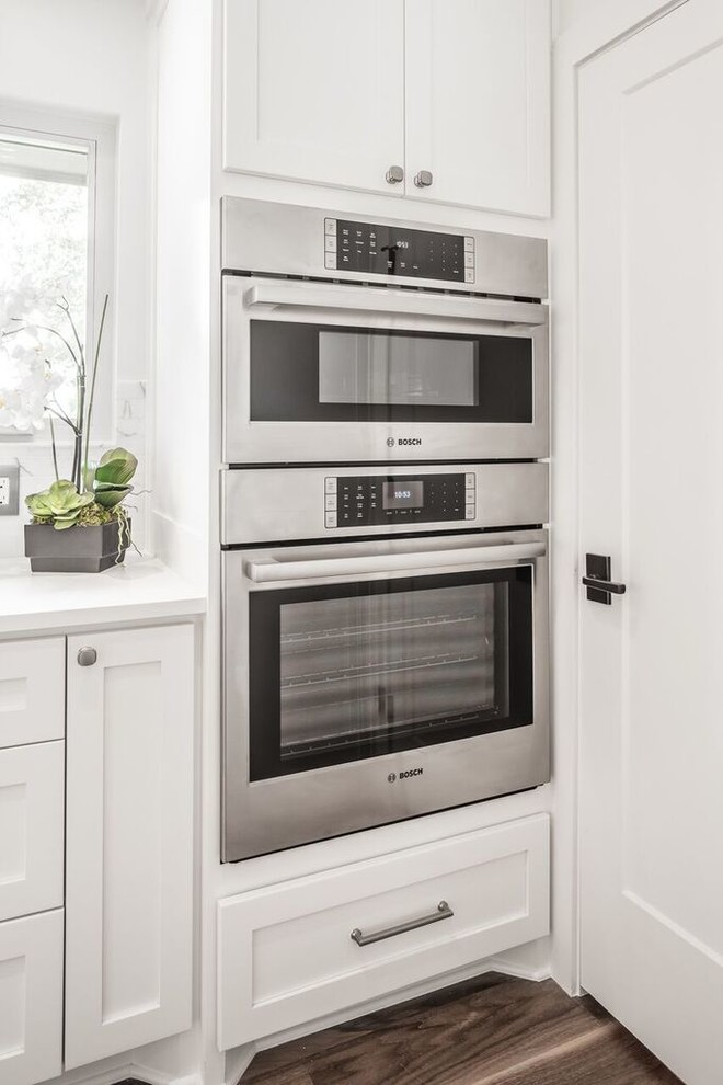 Example of a transitional u-shaped medium tone wood floor enclosed kitchen design in Austin with shaker cabinets, white cabinets, quartz countertops, white backsplash, stone tile backsplash and stainless steel appliances