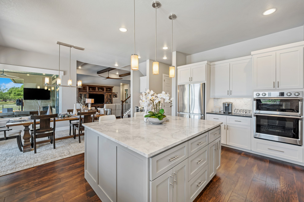 Inspiration for a large traditional u-shaped eat-in kitchen in Tampa with an integrated sink, raised-panel cabinets, white cabinets, marble benchtops, white splashback, porcelain splashback, stainless steel appliances, dark hardwood floors, with island, brown floor and white benchtop.