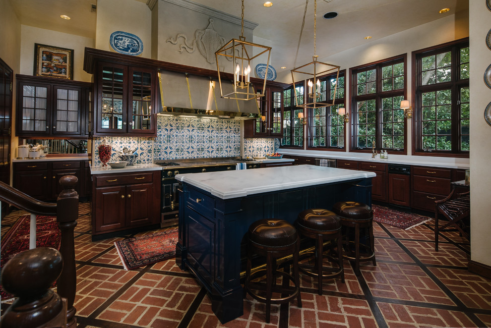 Traditional kitchen in Houston with glass-front cabinets, dark wood cabinets, multi-coloured splashback, black appliances, brick floors and with island.
