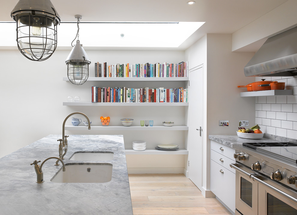 Photo of a large contemporary kitchen in London with flat-panel cabinets, white cabinets, solid surface benchtops, white splashback, stainless steel appliances, with island, a double-bowl sink, subway tile splashback and light hardwood floors.