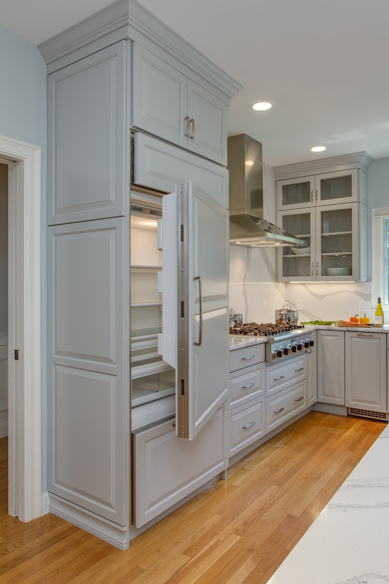 Example of a large transitional l-shaped medium tone wood floor open concept kitchen design in Boston with an undermount sink, raised-panel cabinets, gray cabinets, quartz countertops, stone slab backsplash, paneled appliances and an island