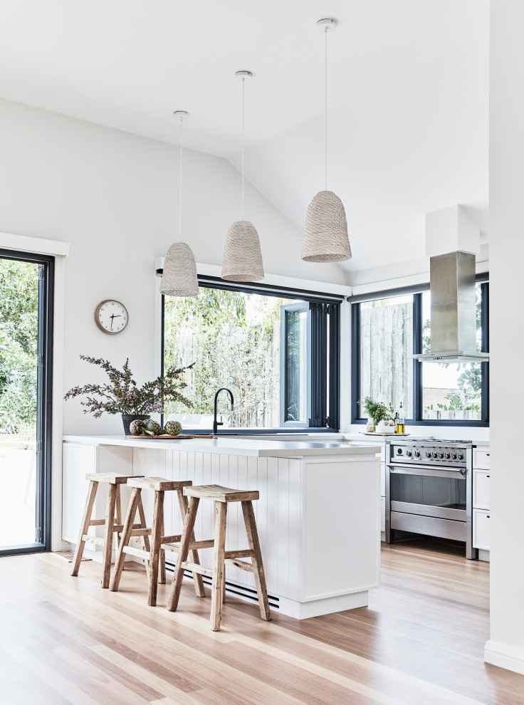 Mid-sized beach style u-shaped eat-in kitchen in Sydney with a double-bowl sink, shaker cabinets, white cabinets, quartz benchtops, window splashback, stainless steel appliances, light hardwood floors, a peninsula and grey benchtop.