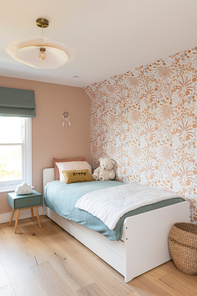 Photo of a medium sized contemporary children’s room for girls in London with pink walls, light hardwood flooring, beige floors, wallpapered walls and a feature wall.
