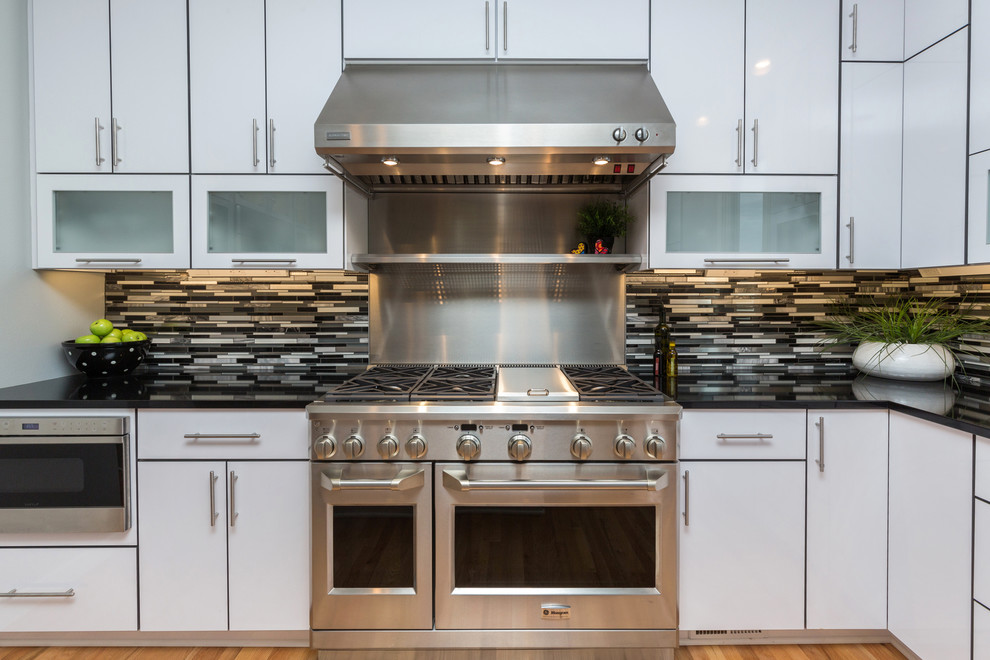 Example of a large trendy u-shaped light wood floor open concept kitchen design with an undermount sink, flat-panel cabinets, white cabinets, granite countertops, multicolored backsplash, mosaic tile backsplash, stainless steel appliances and an island