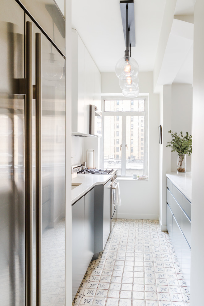 This is an example of a small transitional galley kitchen in New York with a double-bowl sink, flat-panel cabinets, grey cabinets, quartz benchtops, white splashback, stainless steel appliances, terra-cotta floors, white floor and white benchtop.