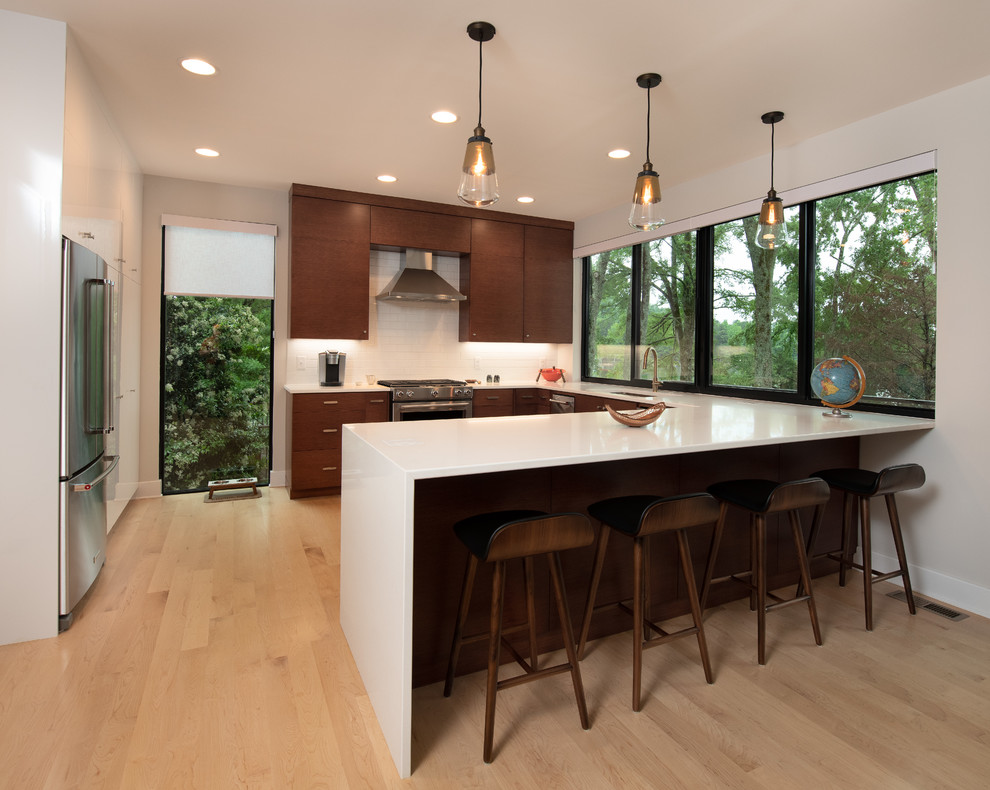Photo of a mid-sized midcentury u-shaped eat-in kitchen in Other with an undermount sink, flat-panel cabinets, medium wood cabinets, quartz benchtops, white splashback, ceramic splashback, stainless steel appliances, light hardwood floors, a peninsula, beige floor and white benchtop.