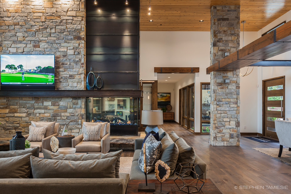 Expansive contemporary open concept living room in Portland with dark hardwood floors, a two-sided fireplace, a stone fireplace surround and a wall-mounted tv.