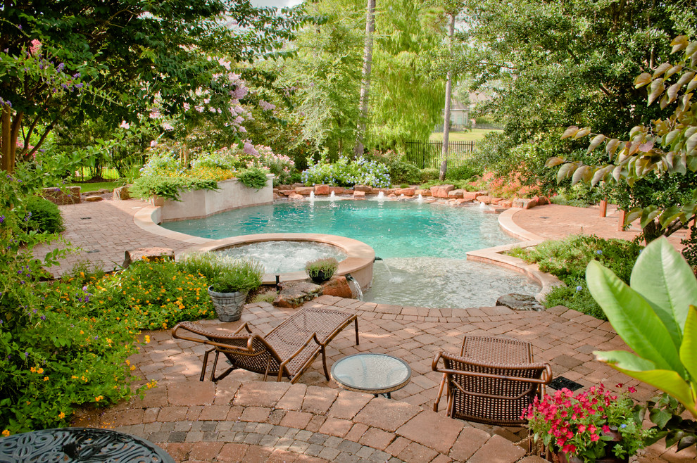 This is an example of a large traditional backyard round pool in Houston with natural stone pavers and a hot tub.