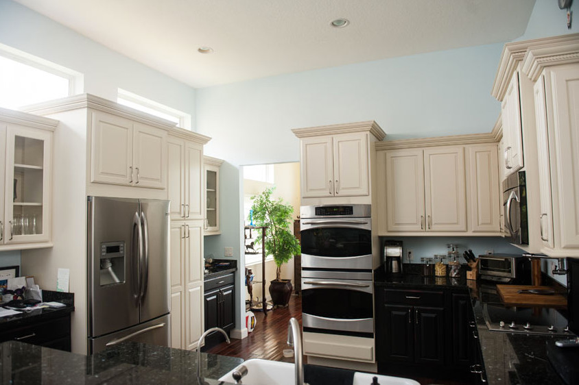 Inspiration for a large transitional u-shaped dark wood floor eat-in kitchen remodel in Miami with a farmhouse sink, flat-panel cabinets, black cabinets, granite countertops, blue backsplash, stainless steel appliances and a peninsula
