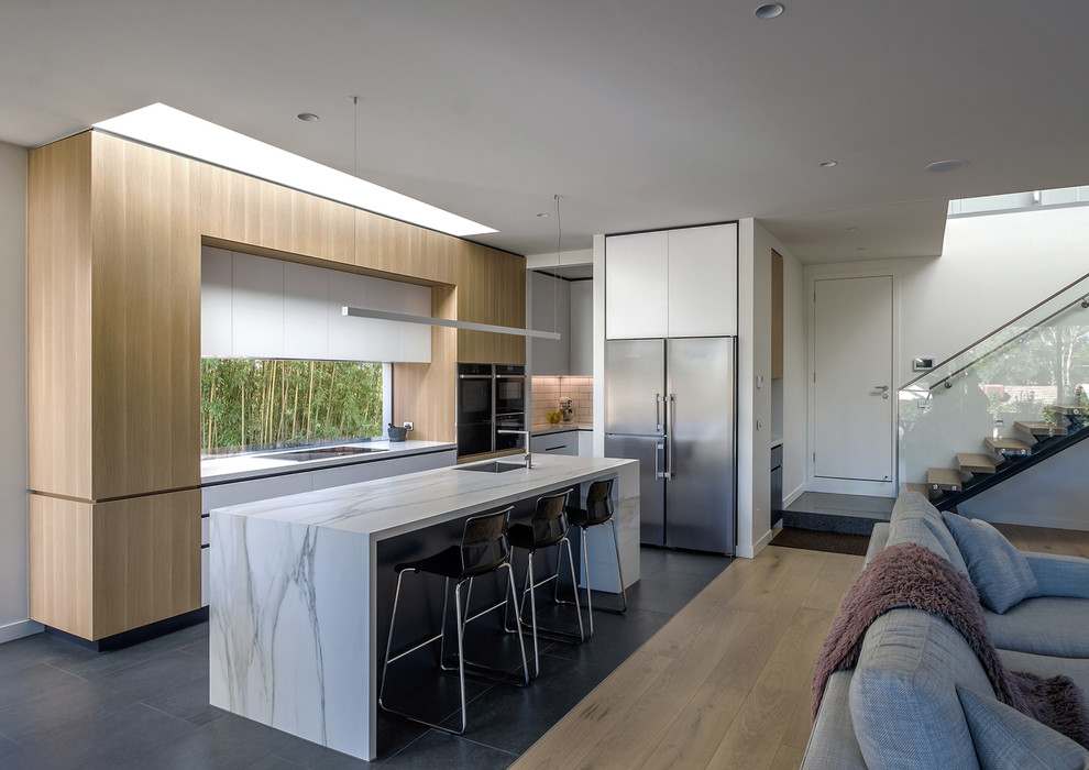 Mid-sized modern galley open plan kitchen in Melbourne with an undermount sink, flat-panel cabinets, medium wood cabinets, quartz benchtops, stainless steel appliances, porcelain floors, with island, grey floor and white benchtop.