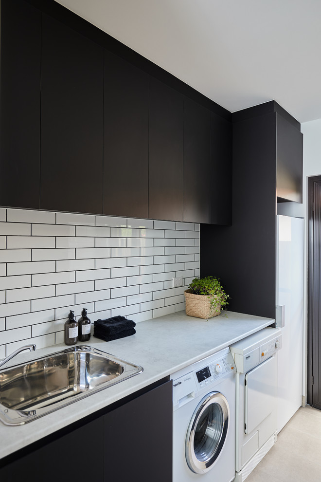 Photo of a mid-sized scandinavian galley dedicated laundry room in Melbourne with a drop-in sink, black cabinets, laminate benchtops, white walls, a side-by-side washer and dryer, grey floor and grey benchtop.