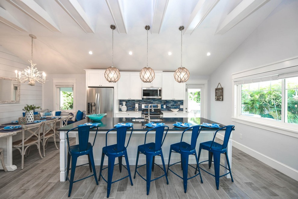 Beach style eat-in kitchen in Tampa with an undermount sink, shaker cabinets, white cabinets, quartzite benchtops, blue splashback, glass tile splashback, stainless steel appliances, porcelain floors, with island, grey floor and blue benchtop.