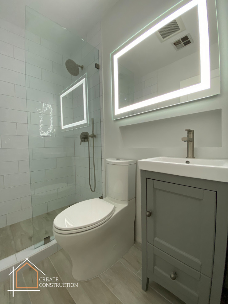 This is an example of a small modern shower room bathroom in Los Angeles with recessed-panel cabinets, grey cabinets, a walk-in shower, a one-piece toilet, white tiles, ceramic tiles, white walls, ceramic flooring, an integrated sink, marble worktops, grey floors, an open shower, white worktops, a wall niche, a single sink and a freestanding vanity unit.