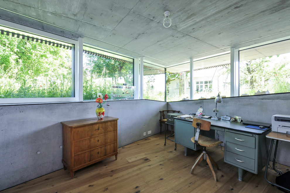 Industrial home studio in Milan with medium hardwood floors, a freestanding desk, no fireplace, grey walls and brown floor.
