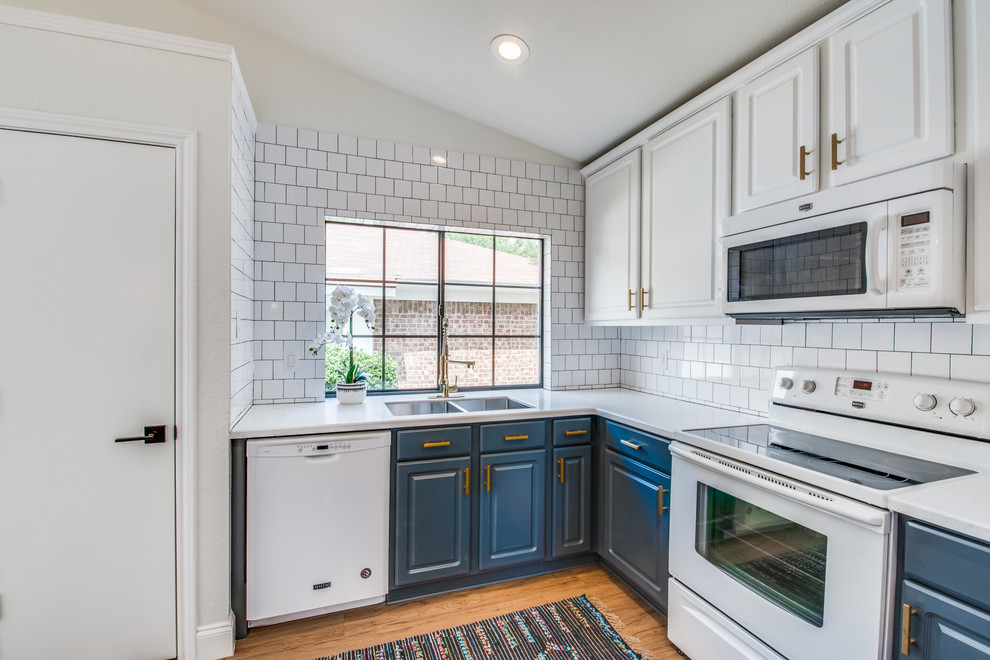 Photo of a midcentury u-shaped eat-in kitchen in Dallas with an undermount sink, raised-panel cabinets, blue cabinets, quartz benchtops, white splashback, subway tile splashback, white appliances, light hardwood floors, brown floor and white benchtop.