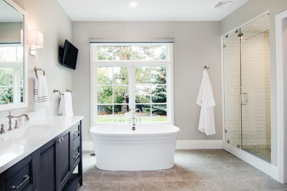 Inspiration for a large transitional master bathroom in Denver with recessed-panel cabinets, dark wood cabinets, a freestanding tub, a corner shower, a one-piece toilet, white tile, ceramic tile, grey walls, porcelain floors, a drop-in sink, engineered quartz benchtops, grey floor and a hinged shower door.