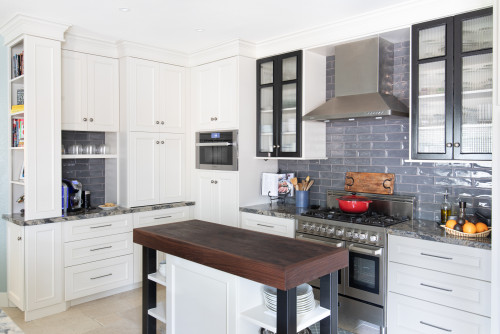Bright kitchen with white shaker RTA cabinets, black-framed glass uppers, glossy gray subway tile backsplash, stainless range and hood, and a slim wood-top island.