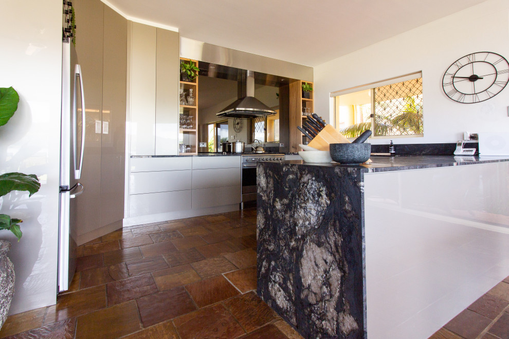 Inspiration for a large modern u-shaped kitchen pantry in Central Coast with a double-bowl sink, flat-panel cabinets, beige cabinets, granite benchtops, metallic splashback, glass sheet splashback, stainless steel appliances, slate floors, a peninsula, brown floor and black benchtop.