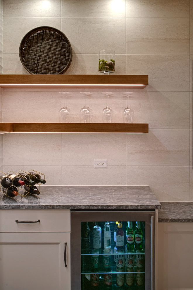 This is an example of a medium sized single-wall dry bar in Chicago with no sink, floating shelves, white cabinets, quartz worktops, beige splashback, ceramic splashback, carpet, grey floors and grey worktops.