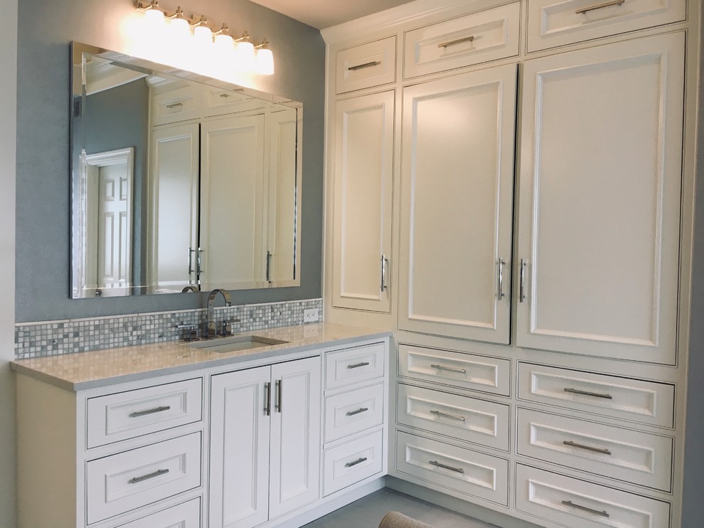 Photo of a large transitional master bathroom in Kansas City with raised-panel cabinets, white cabinets, a freestanding tub, a curbless shower, a two-piece toilet, white tile, marble, grey walls, ceramic floors, an undermount sink, quartzite benchtops, grey floor, a hinged shower door and grey benchtops.