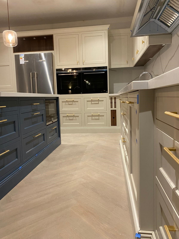 Example of a large classic l-shaped open concept kitchen design in London with a drop-in sink, shaker cabinets, white cabinets, quartzite countertops, white backsplash, stone slab backsplash, stainless steel appliances, an island and white countertops
