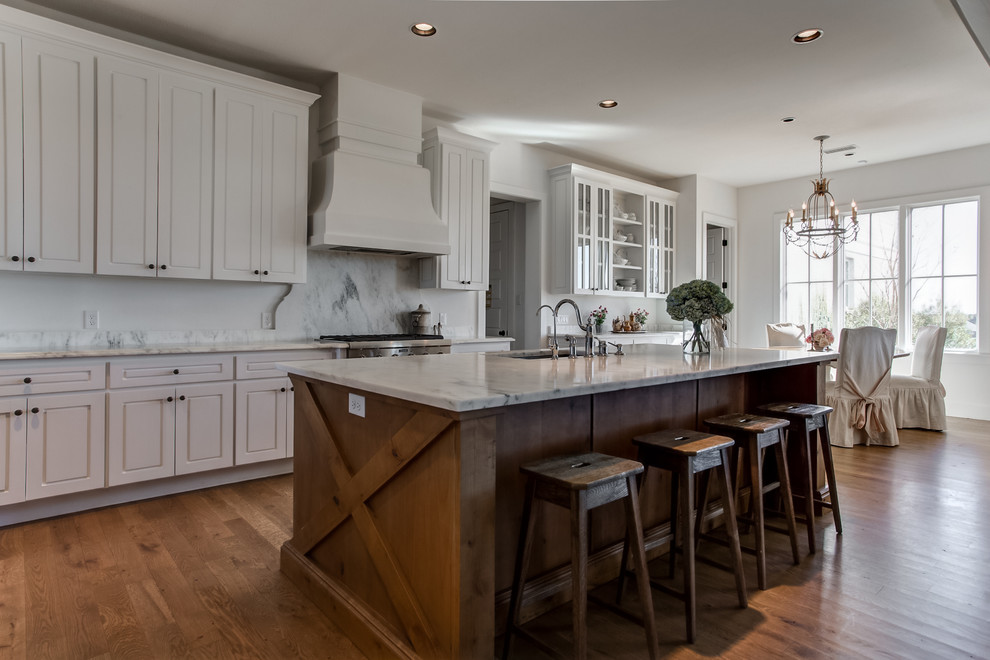 This is an example of a mid-sized traditional single-wall eat-in kitchen in Dallas with an undermount sink, raised-panel cabinets, white cabinets, marble benchtops, multi-coloured splashback, stone slab splashback, stainless steel appliances, light hardwood floors and with island.