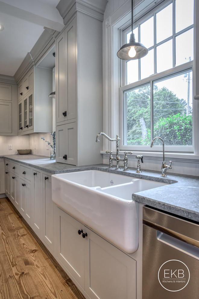 This is an example of a mid-sized traditional u-shaped eat-in kitchen in New York with a farmhouse sink, shaker cabinets, grey cabinets, soapstone benchtops, white splashback, timber splashback, stainless steel appliances, medium hardwood floors, no island, brown floor and multi-coloured benchtop.