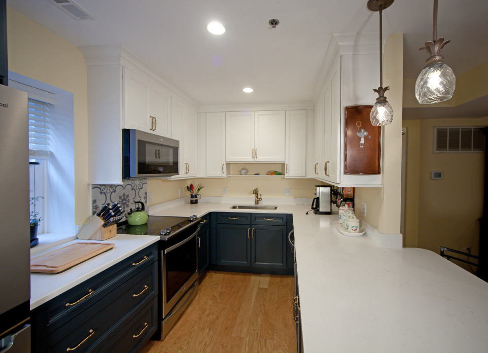 Design ideas for a small transitional u-shaped kitchen in Philadelphia with a single-bowl sink, shaker cabinets, blue cabinets, marble benchtops, stainless steel appliances, light hardwood floors, a peninsula, brown floor and white benchtop.