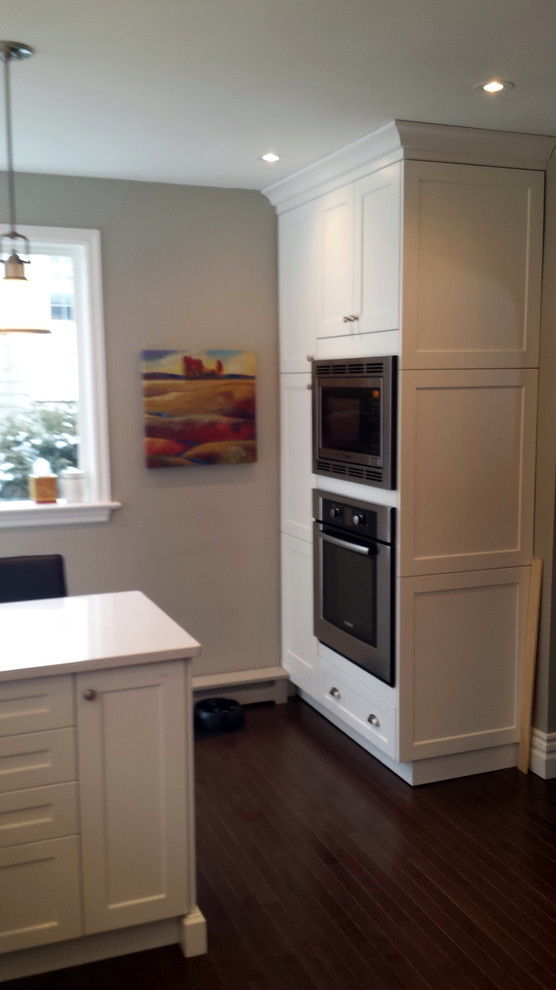 Inspiration for a mid-sized transitional u-shaped dark wood floor enclosed kitchen remodel in Ottawa with an undermount sink, shaker cabinets, white cabinets, quartz countertops, white backsplash, subway tile backsplash, stainless steel appliances and a peninsula
