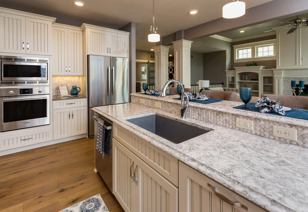 Kitchen pantry - transitional l-shaped kitchen pantry idea with an undermount sink, beaded inset cabinets, white cabinets, quartz countertops, beige backsplash, stone tile backsplash, stainless steel appliances and an island