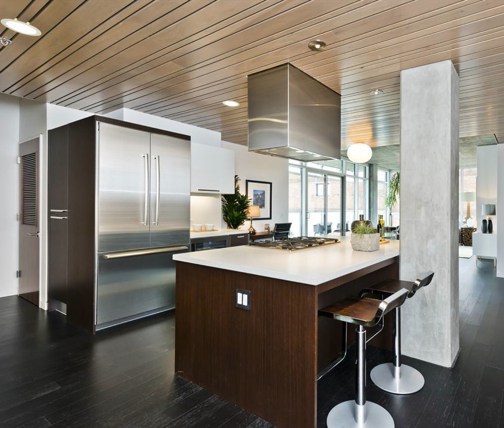 This is an example of a mid-sized contemporary u-shaped open plan kitchen in San Francisco with stainless steel appliances, flat-panel cabinets, dark wood cabinets, quartz benchtops, white splashback, with island, an integrated sink and dark hardwood floors.