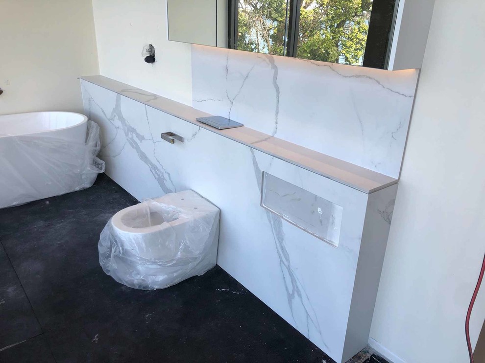 Design ideas for a large modern master bathroom in Sydney with a freestanding tub, white tile, porcelain tile, porcelain floors, solid surface benchtops, black floor and white benchtops.