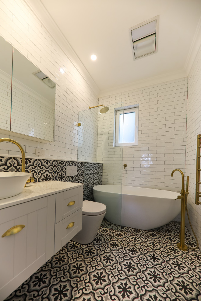 Photo of a small eclectic master bathroom in Sydney with beaded inset cabinets, white cabinets, a freestanding tub, an open shower, a one-piece toilet, white tile, subway tile, white walls, cement tiles, a vessel sink, engineered quartz benchtops, black floor, an open shower, white benchtops, an enclosed toilet, a single vanity, a floating vanity, coffered and brick walls.