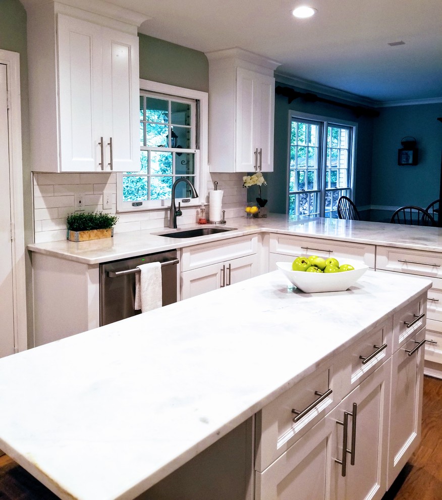 Large transitional u-shaped medium tone wood floor and brown floor enclosed kitchen photo in Miami with an undermount sink, shaker cabinets, white cabinets, quartz countertops, white backsplash, subway tile backsplash, stainless steel appliances, an island and white countertops
