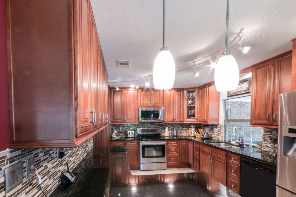 Mid-sized l-shaped kitchen photo with an undermount sink, raised-panel cabinets, medium tone wood cabinets, granite countertops, glass tile backsplash, stainless steel appliances and black countertops
