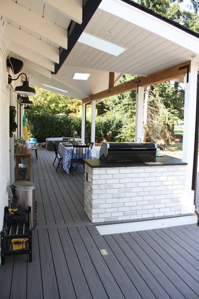 This is an example of a large country backyard deck in Seattle with an outdoor kitchen and a roof extension.