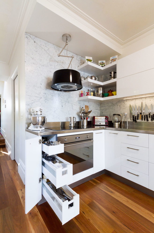 Design ideas for a small contemporary l-shaped kitchen pantry in Melbourne with an integrated sink, flat-panel cabinets, white cabinets, stainless steel benchtops, white splashback, marble splashback, stainless steel appliances, medium hardwood floors and brown floor.