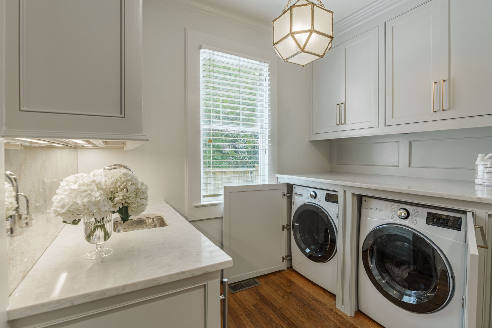 Design ideas for a small transitional galley utility room in Other with beaded inset cabinets, grey cabinets, marble benchtops, metallic splashback, mirror splashback, white walls, dark hardwood floors, a side-by-side washer and dryer, brown floor and white benchtop.
