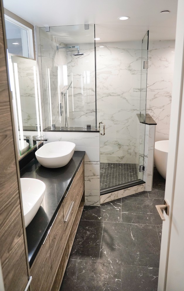This is an example of a mid-sized modern master bathroom in San Diego with flat-panel cabinets, light wood cabinets, a freestanding tub, a corner shower, a bidet, multi-coloured tile, porcelain tile, white walls, porcelain floors, a vessel sink, quartzite benchtops, black floor, a hinged shower door and black benchtops.