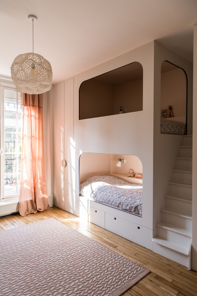 This is an example of a contemporary kids' bedroom for girls in Paris with beige walls, medium hardwood flooring and brown floors.